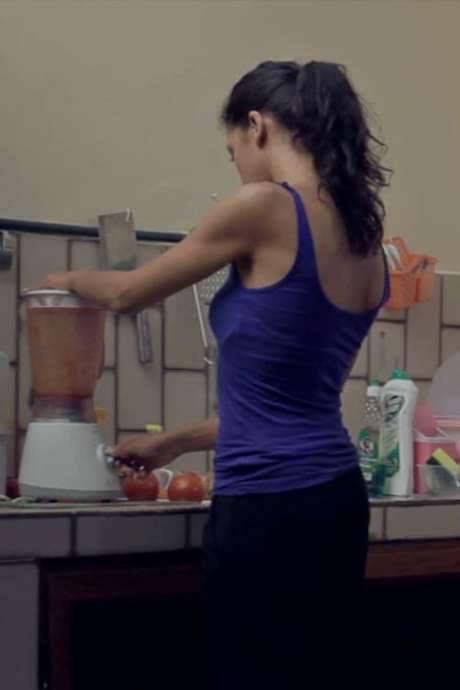    A woman is making dinner in the kitchen, which disturbs her husband who is watching TV.  